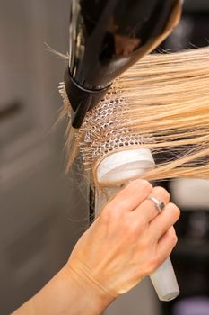 Close up of hairdresser's hand is drying hair of the blonde young woman in a hair salon
