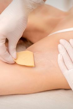 Close up of hands in gloves of beautician waxing young female armpit with sugar paste in hair removal salon