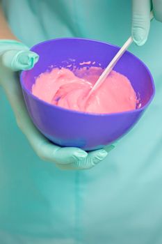 Close up of beautician's hands prepares pink alginate mask mixing in the blue bowl