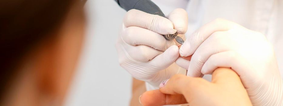 Closeup of manicure master removes nail polish uses an electric nail file in a nail salon