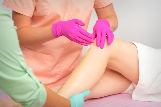 Hands of a beautician in pink gloves epilating leg of a young female in hair removal salon