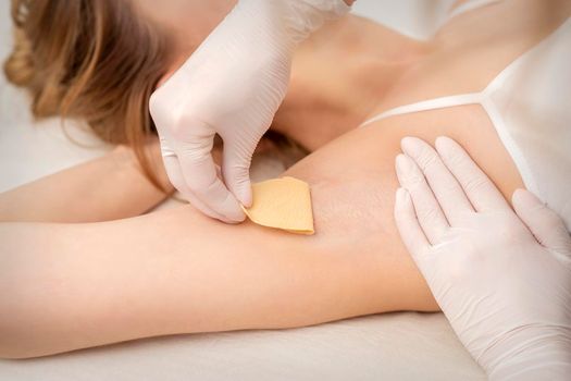 Close up of hands in gloves of beautician waxing young female armpit with sugar paste in hair removal salon