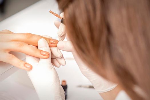 Manicurist applying beige nail polish on fingernails of a female client in a nail salon