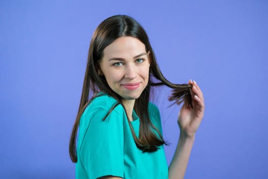 Young woman with long shiny hairstyle looking to camera, flirting. Beautiful model girl on violet studio background. High quality photo