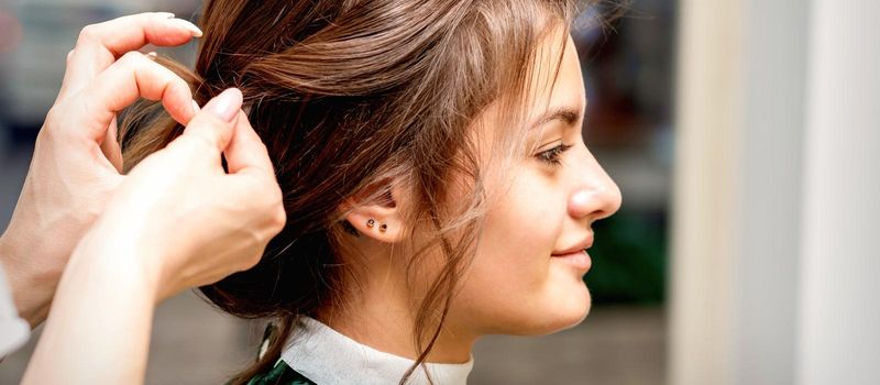 Side view of hands of hair stylist styling hair of the beautiful young caucasian brunette woman in a beauty salon