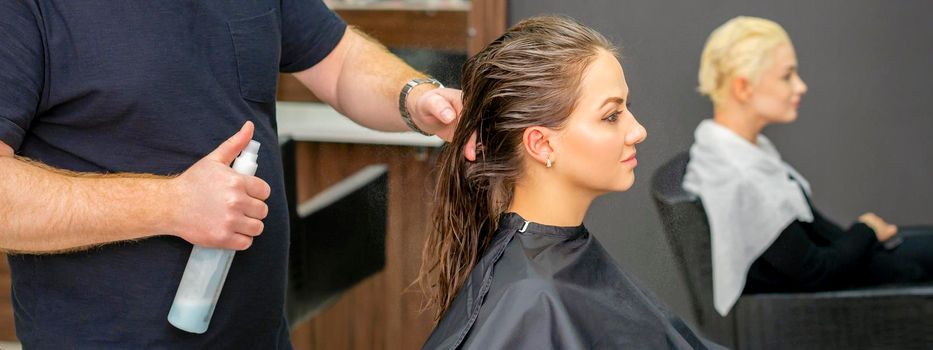 Male hairdresser sprays water long wet hair of a young woman in a hair salon