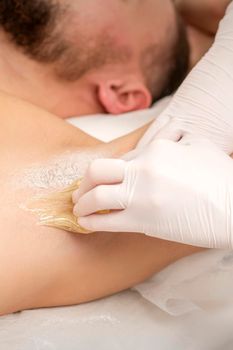 Close up of hands in gloves of beautician waxing young male armpit with sugar paste in hair removal salon