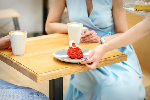 The waiter's hand puts on the table a plate with a red cupcake on the background of a female client in a cafe