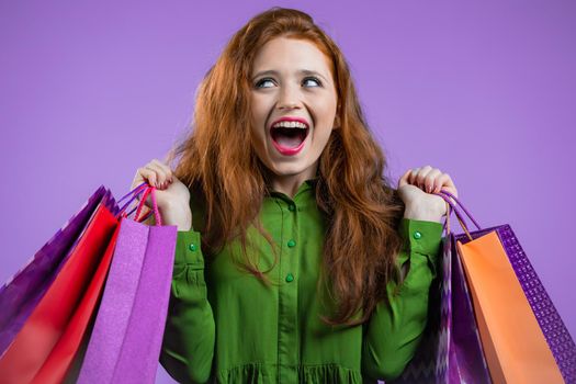 Excited woman with colorful paper bags after shopping on violet studio background. Concept of seasonal sale, purchases, spending money on gifts. High quality photo