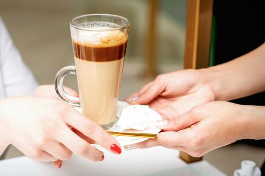 Closeup of woman's hands taking the latte cup from hands of a barista in a coffee shop