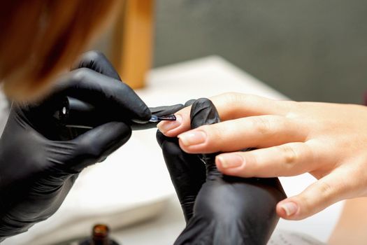 Close up of manicure master covering nails with the transparent polish of female nails in a nail salon