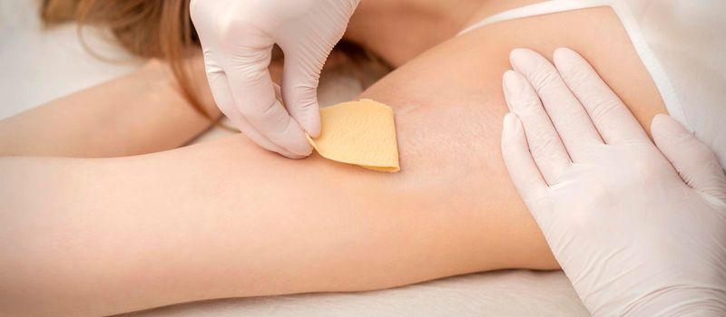 Close up of hands in gloves of beautician waxing young female armpit with sugar paste in hair removal salon