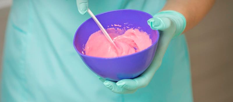 Close up of beautician's hands prepares pink alginate mask mixing in the blue bowl