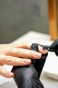 Close up of manicure master covering nails with the transparent polish of female nails in a nail salon