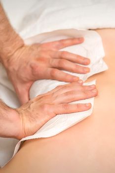 Hands of a masseur with towel massaging back of a young adult woman in spa salon