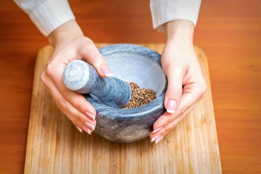 Female hands grind dry pepper spices in mortar on a wooden kitchen board