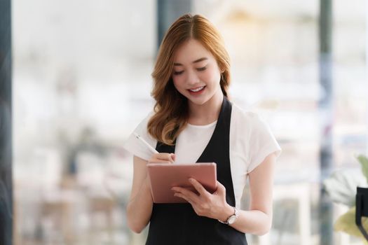 Beautiful Asian women Barista smiling and using tablet at her cafe.