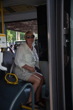 middle-aged caucasian woman sitting in bus pictures through glass with reflection of bus stop and public transport. High quality photo