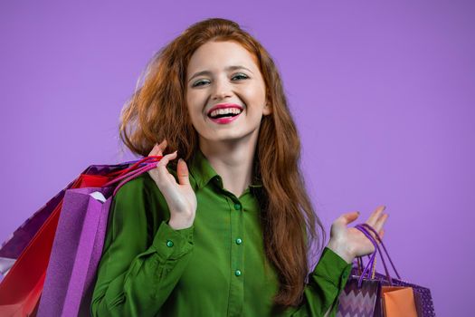 Excited woman with colorful paper bags after shopping on violet studio background. Concept of seasonal sale, purchases, spending money on gifts. High quality photo