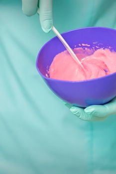 Close up of beautician's hands prepares pink alginate mask mixing in the blue bowl