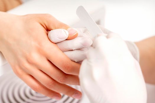 Manicure master wears white gloves with nail file doing manicure on female fingernails in a nail salon