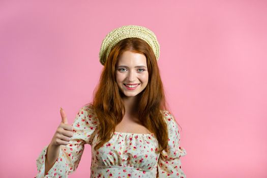 Lady with long hair shows thumbs up, Like gesture. Happy woman on pink background. Winner. Success. Positive girl smiles to camera. Body language