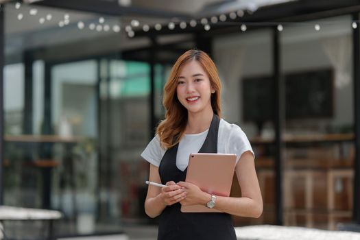 Beautiful Asian women Barista smiling and using tablet at her cafe.