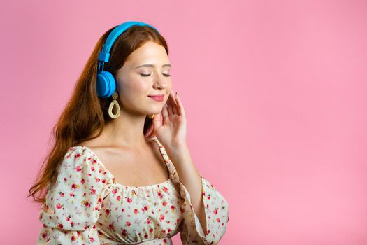 Attractive woman with red hair with headphones on pink studio background. Cute girl portrait. Music, radio, happiness, freedom, youth concept