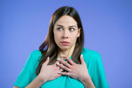 Portrait of unpleasantly surprised and shocked girl on violet studio background. Woman receiving bad news. She expresses sympathy and regret. High quality photo