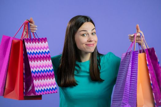 Excited woman with colorful paper bags after shopping on violet studio background. Concept of seasonal sale, purchases, spending money on gifts. High quality photo