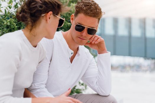 Young couple having problems in their relationship. man and woman friends in sunglasses sitting bench in city unhappy emotions. Relationships problem.