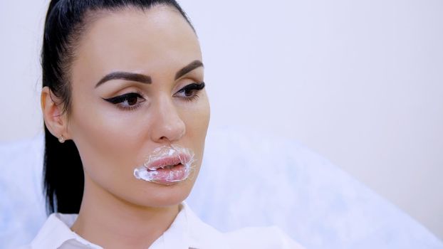 close-up, the patient sits in the cosmetology clinic with a superimposed anesthetic cream pad on the lips, top covered with a polytene film. Lip augmentation procedure. High quality photo