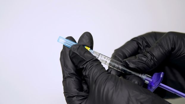 close-up, a sterile syringe with hyaluronic acid in the hands of a doctor dressed in black gloves. High quality photo