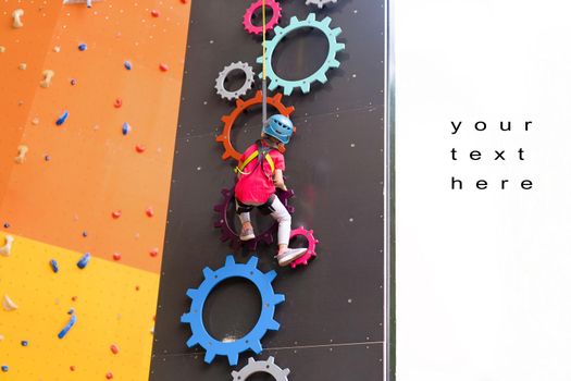 Child climbing on wall in amusement centre. Climbing training for children. Little girl in dressed climbing gear climb high. Extreme active leisure for kids. Caucasian little girl 5 years old.