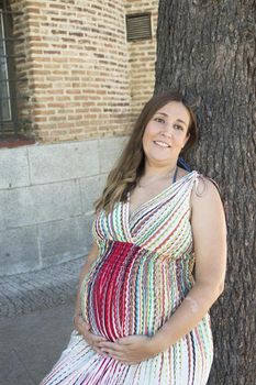 Seven month pregnant woman outdoors in multi colored striped dress. Day scene