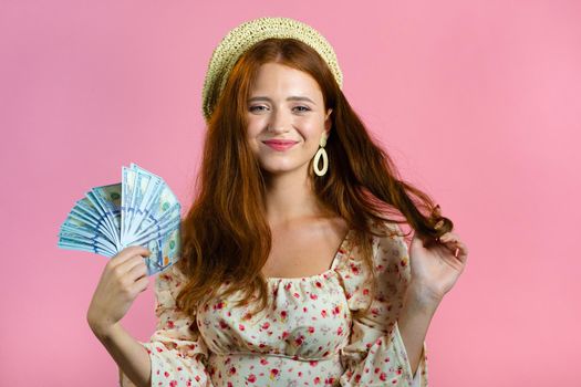 Amazed happy excited woman showing money - U.S. currency dollars banknotes on pink wall. Symbol of success, gain, victory