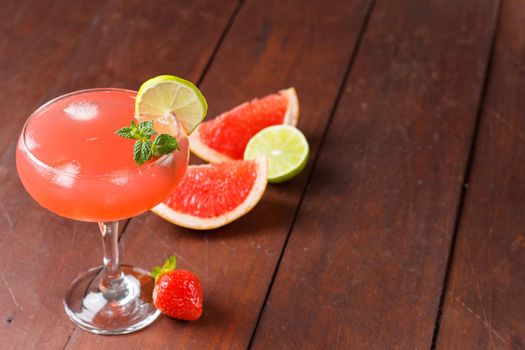 Fresh grapefruit juice in a glass with grapefruit pieces, lime and mint on a wooden background. copy space