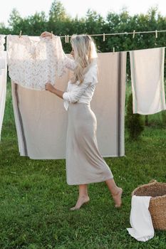 Laundry day. A woman hangs linen and towels on a tree in the courtyard of a village house. Summer cottage concept.