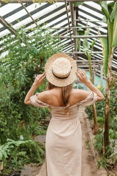 A beautiful young woman takes care of plants in a greenhouse. The concept of gardening and an eco-friendly lifestyle.