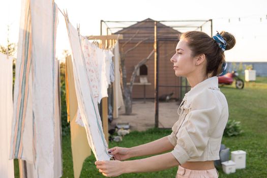 Laundry day. A woman hangs linen and towels on a tree in the courtyard of a village house. Summer cottage concept.