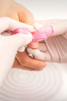 Closeup of manicurist is brushing dust with a pink plastic brush from female fingernails in a nail salon