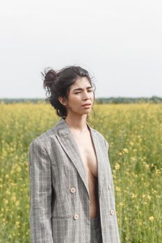 An Asian model poses in a field of yellow flowers for a clothing brand, polyethylene is the main props for a photo shoot. The concept of manufacturing clothing from recycled plastic. A woman in a pantsuit is standing on a plastic bag.