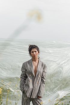 An Asian model poses in a field of yellow flowers for a clothing brand, polyethylene is the main props for a photo shoot. The concept of manufacturing clothing from recycled plastic. A woman in a pantsuit is standing on a plastic bag.