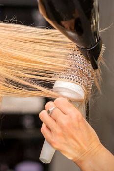 Close up of hairdresser's hand is drying hair of the blonde young woman in a hair salon