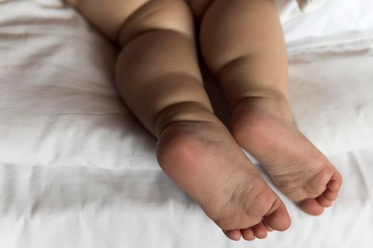 feet of toddler baby girl wearing diapers lying on white bed at home. plump legs of sleeping one year old caucasian child. kid sleeps in crib. home, comfort, childhood, care, love, sweet dream concept.