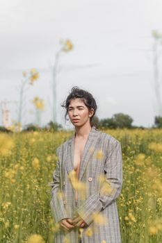 An Asian model poses in a field of yellow flowers for a clothing brand, polyethylene is the main props for a photo shoot. The concept of manufacturing clothing from recycled plastic. A woman in a pantsuit is standing on a plastic bag.