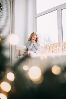 A beautiful blonde girl is sitting on the windowsill with a gray rabbit in a Christmas atmosphere. The concept of pet care.