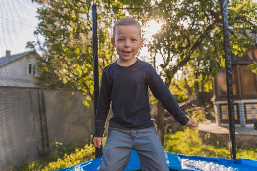 little boy jumps on a trampoline that stands in the yard