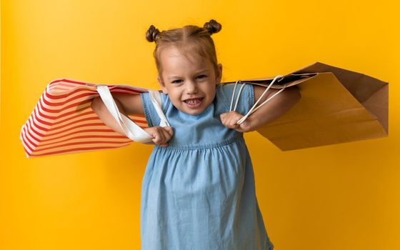 Portrait Caucasian Beautiful Happy Little Preschool Girl Smiling Cheerful And Holding Heavy Cardboard Bags Isolated On Orange Yellow Background. Happiness, Consumerism, Sale People shopping Concept.