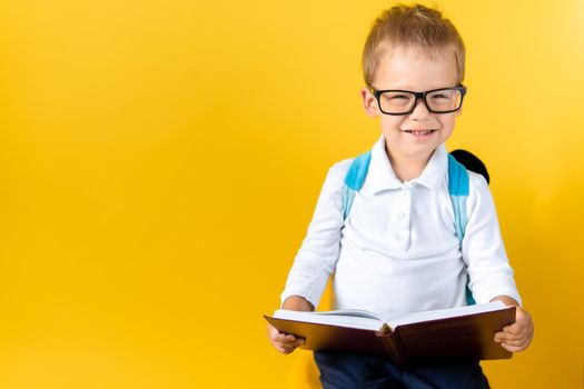 Banner Funny Preschool Child Boy in Big Glasses Reads Book on Yellow Background Copy Space. Happy Smiling Kid Go Back to School, Kindergarten. Success, Motivation, Winner, Genius, Superhero concept.